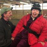 Woman with disabilities riding on a horse with a man standing by